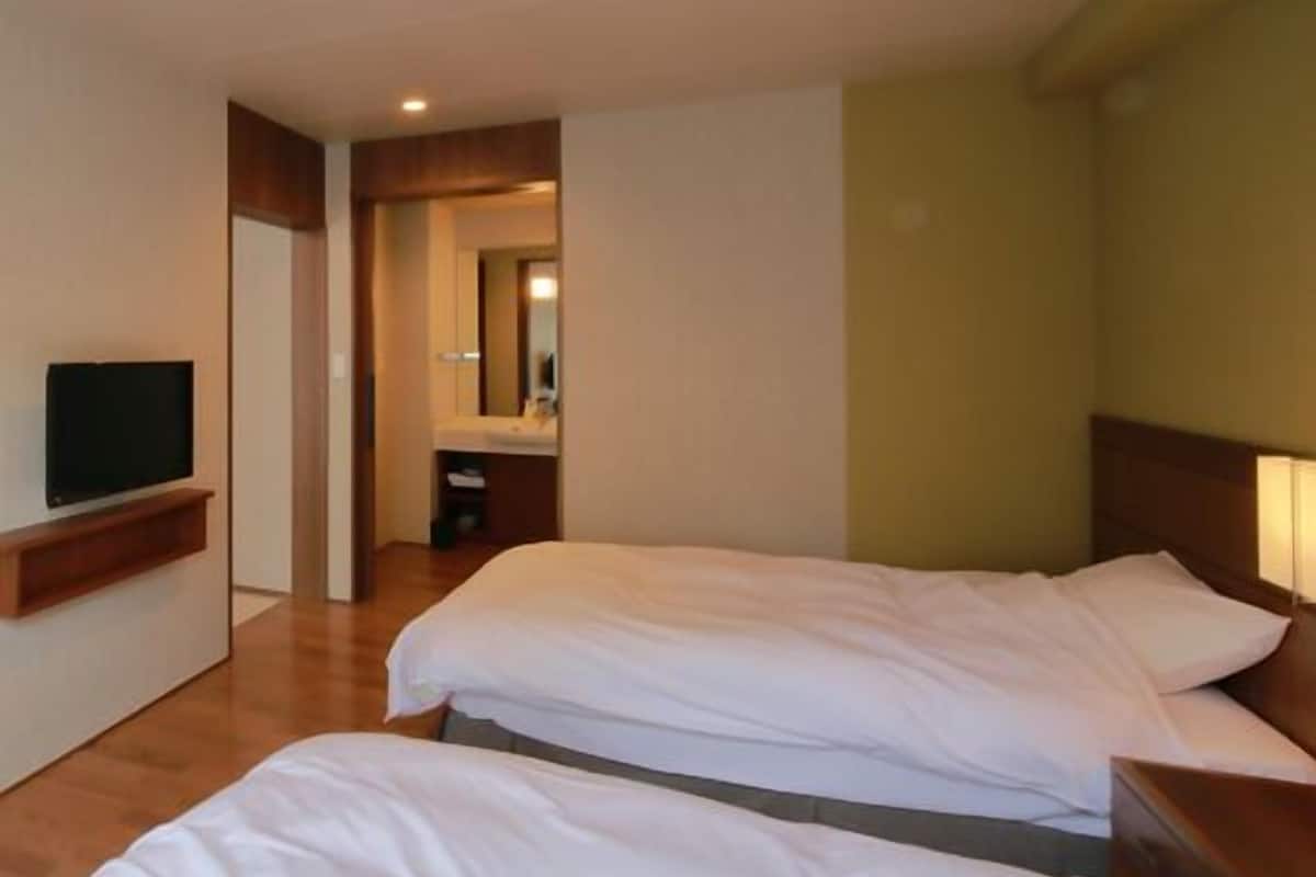 Ein Hotelzimmer mit zwei Betten, einem Fernseher, einem Spiegel und einem durchgegangenes Badezimmer.