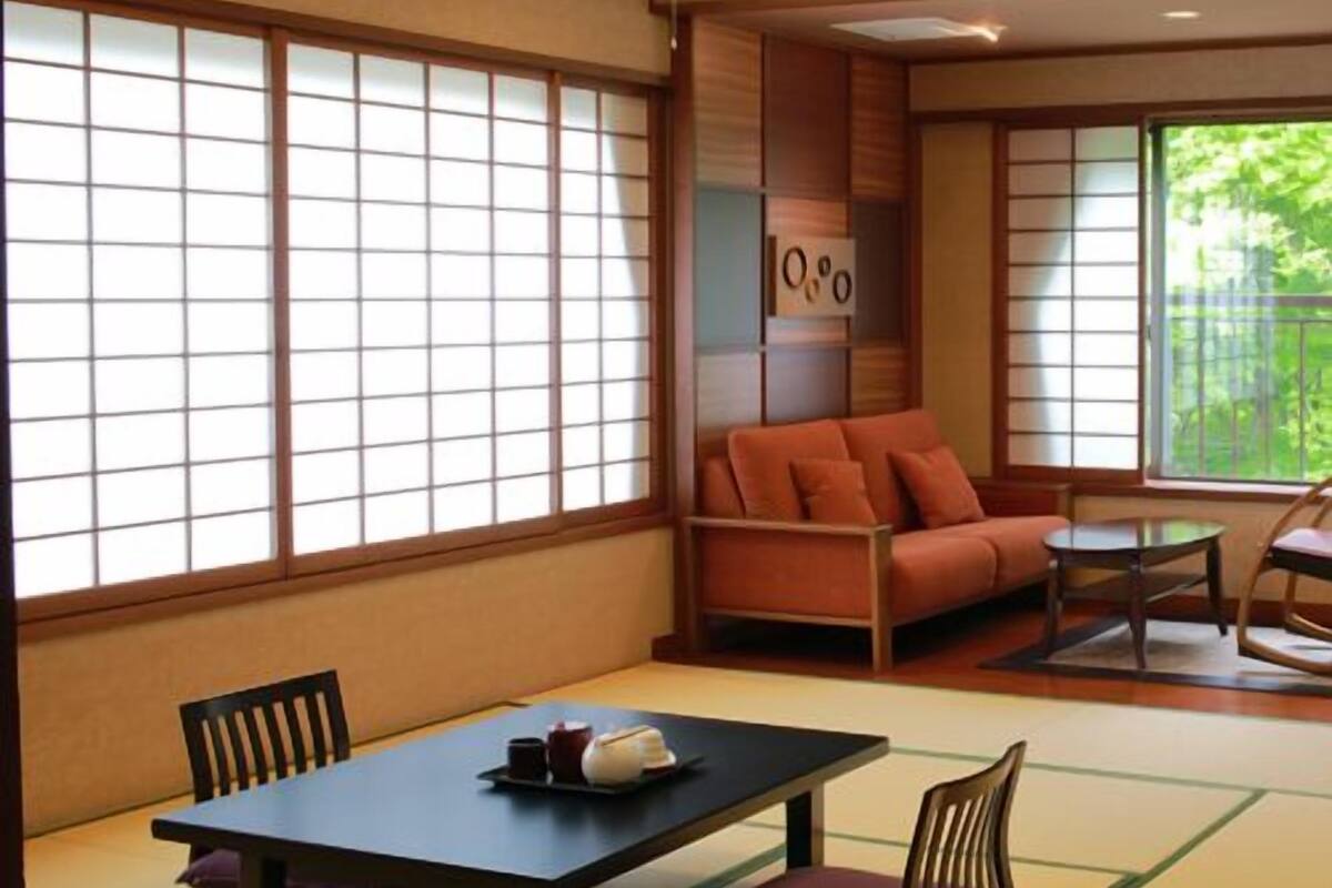 Ein traditioneller japanischer Raum mit Tatami-Bodenbelag, einem niedrigen Tisch mit Kissen, einer Couch und verschiebbaren Shoji-Schiebetüren.