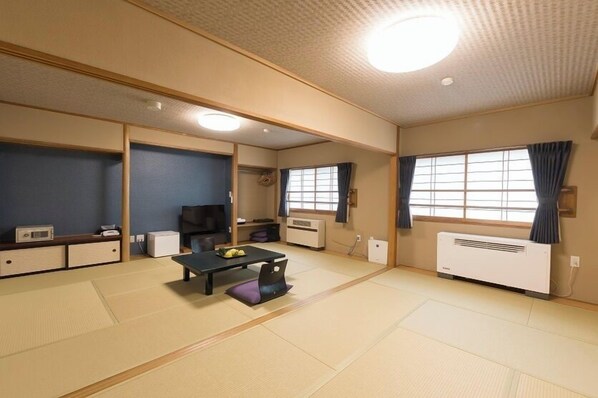 A traditional Japanese room with tatami flooring, a low table with cushions, a television, and a heater. - Okunikko Yumoto Onsen Okunikko Kogen Hotel (Nikko)