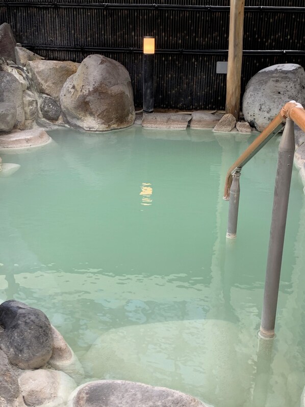 Un área de aguas termales con agua cristalina, rocas grandes y escalones de madera que conducen al agua.