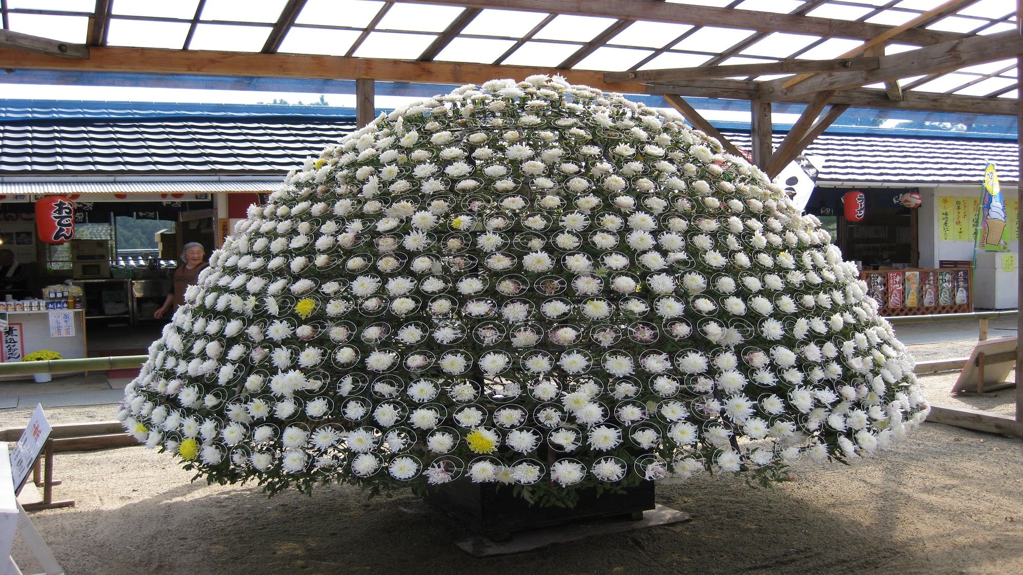 A large spherical floral arrangement in an outdoor setting with a covered structure overhead.