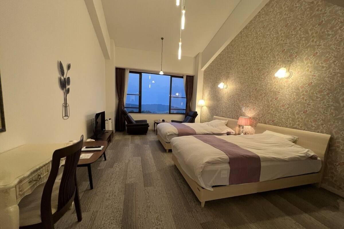 A hotel room with a bed, desk, chair, and a view through the window.