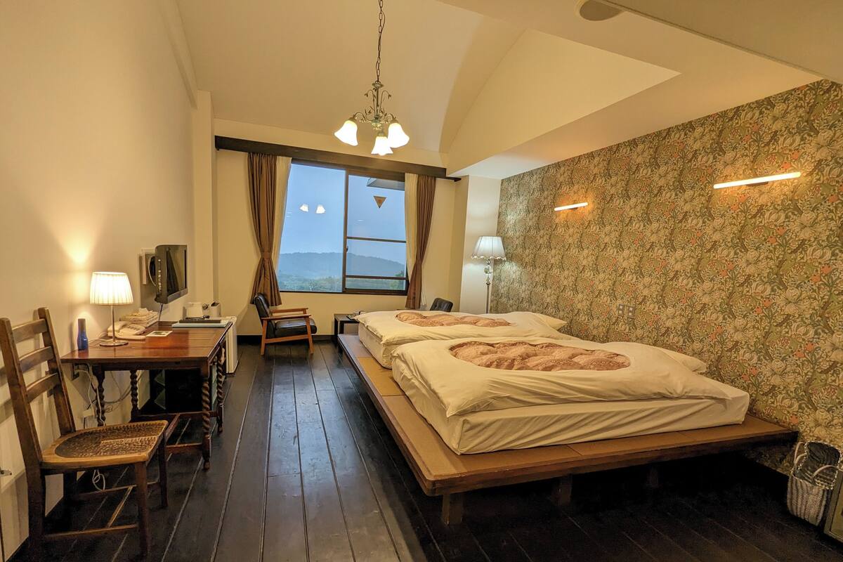 A hotel room with a bed, a desk, a chair, a lamp, a television, and a window with a view.