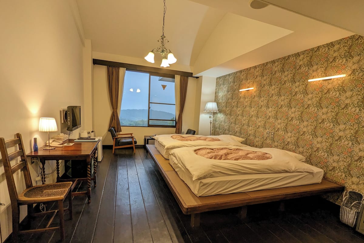A hotel room with a bed, a desk, a chair, a lamp, a television, and a window with a view.