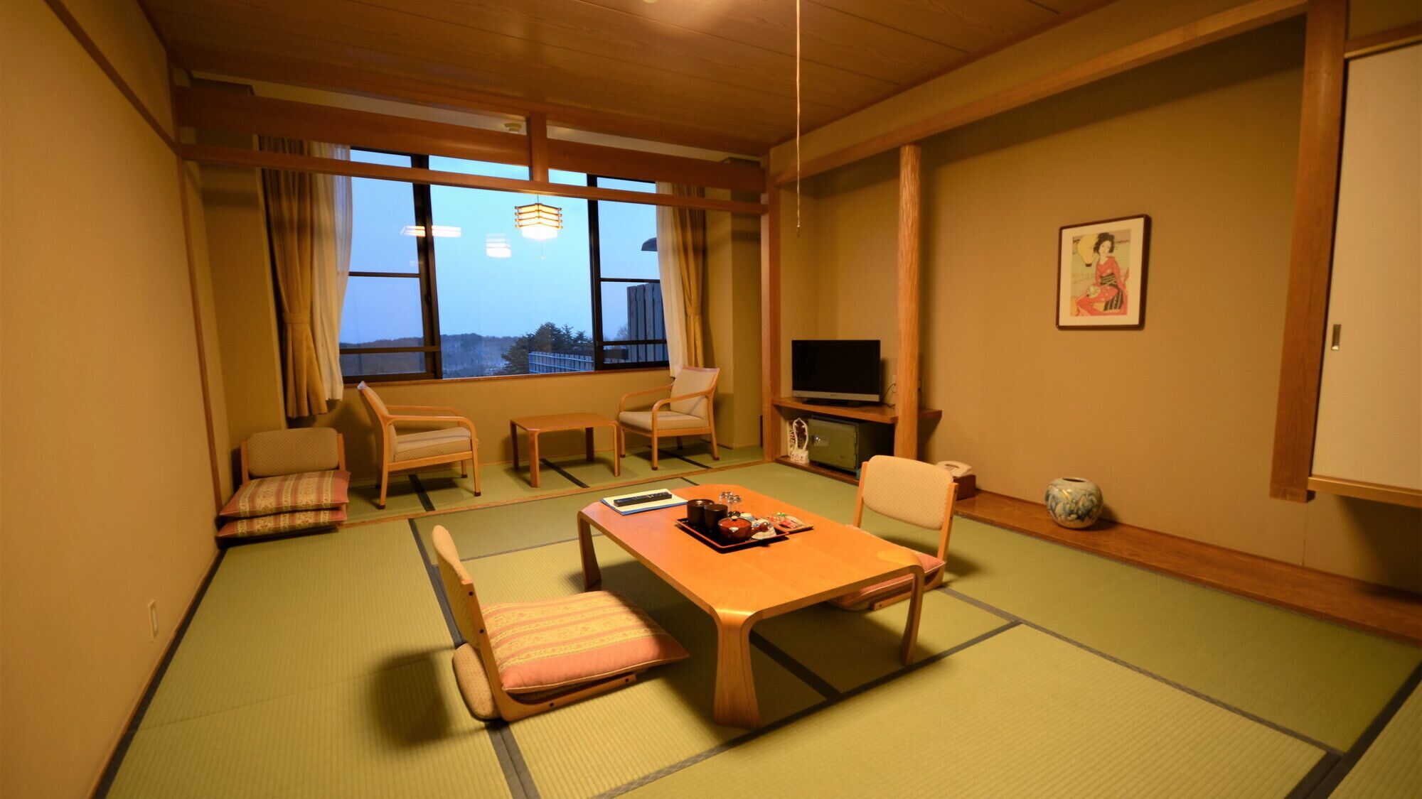 A traditional Japanese-style room with tatami flooring, a low table, two chairs, a television, and a view through large windows.