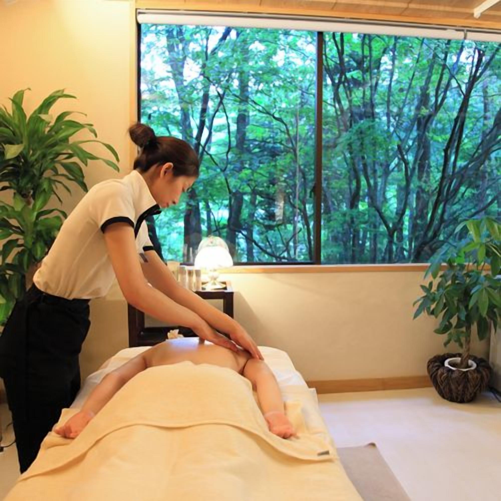 A massage therapy session in a room with a large window overlooking a forest.