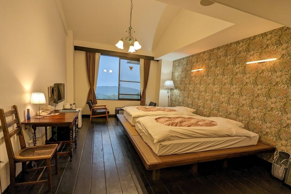 A bedroom with a bed, a desk, a chair, a window with curtains, and a view of the outdoors.