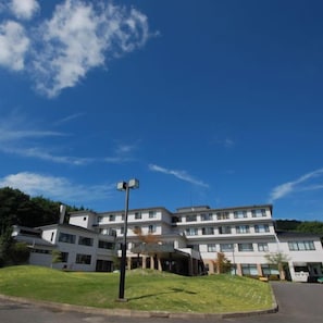 Un edificio de varios pisos con techo plano, estacionamiento y un área verde al frente.