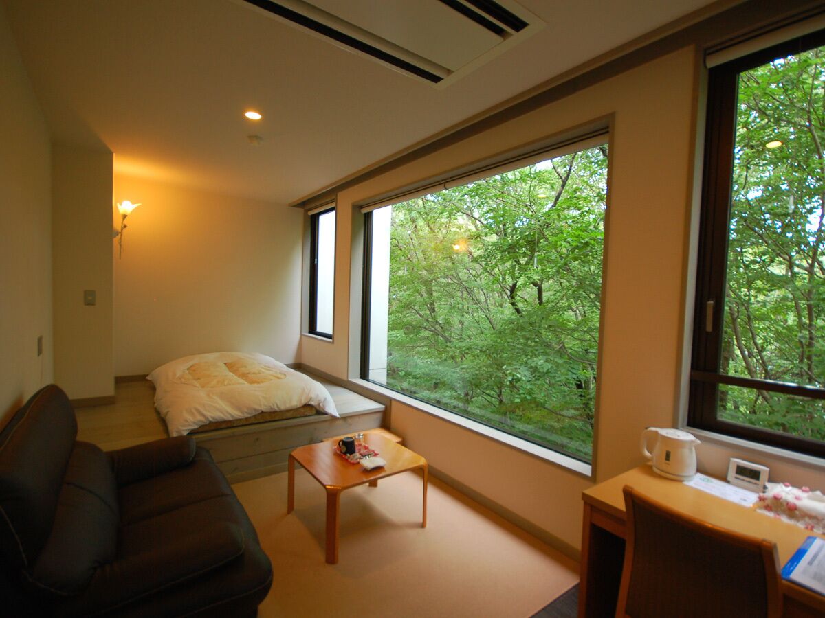 A room with a bed, a sofa, a coffee table, a desk, and a window with a view of trees.