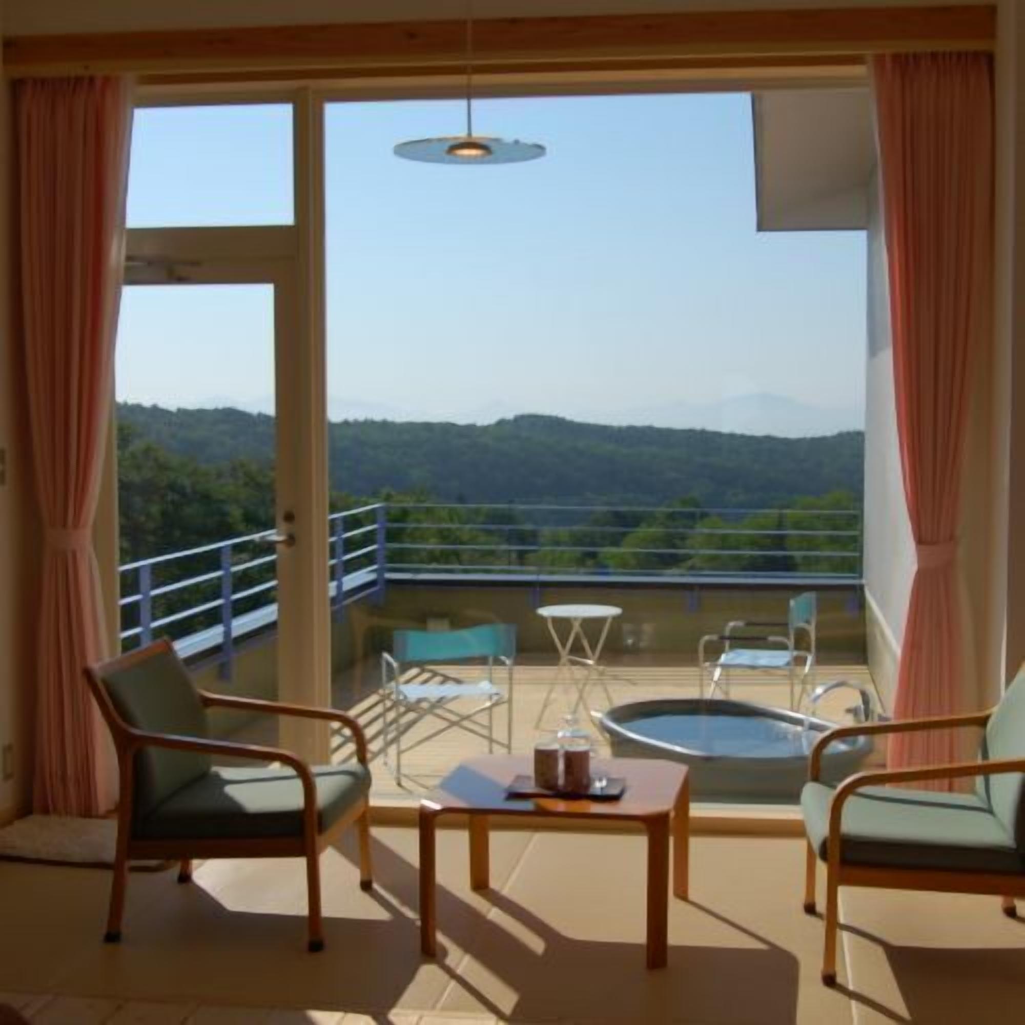 A balcony with a view of a mountainous landscape, furnished with chairs and a table.