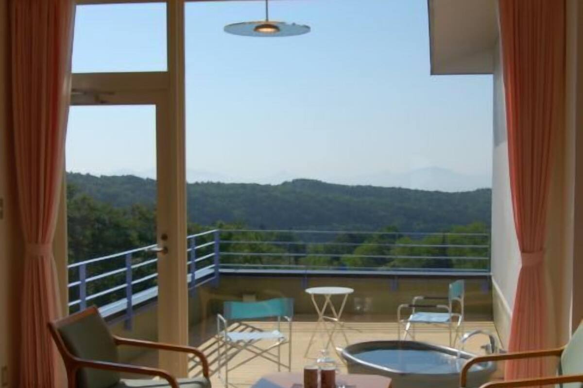 A balcony with a view of a mountainous landscape, furnished with chairs and a table.