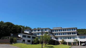 A multi-story building with a flat roof, surrounded by greenery and a clear sky.
