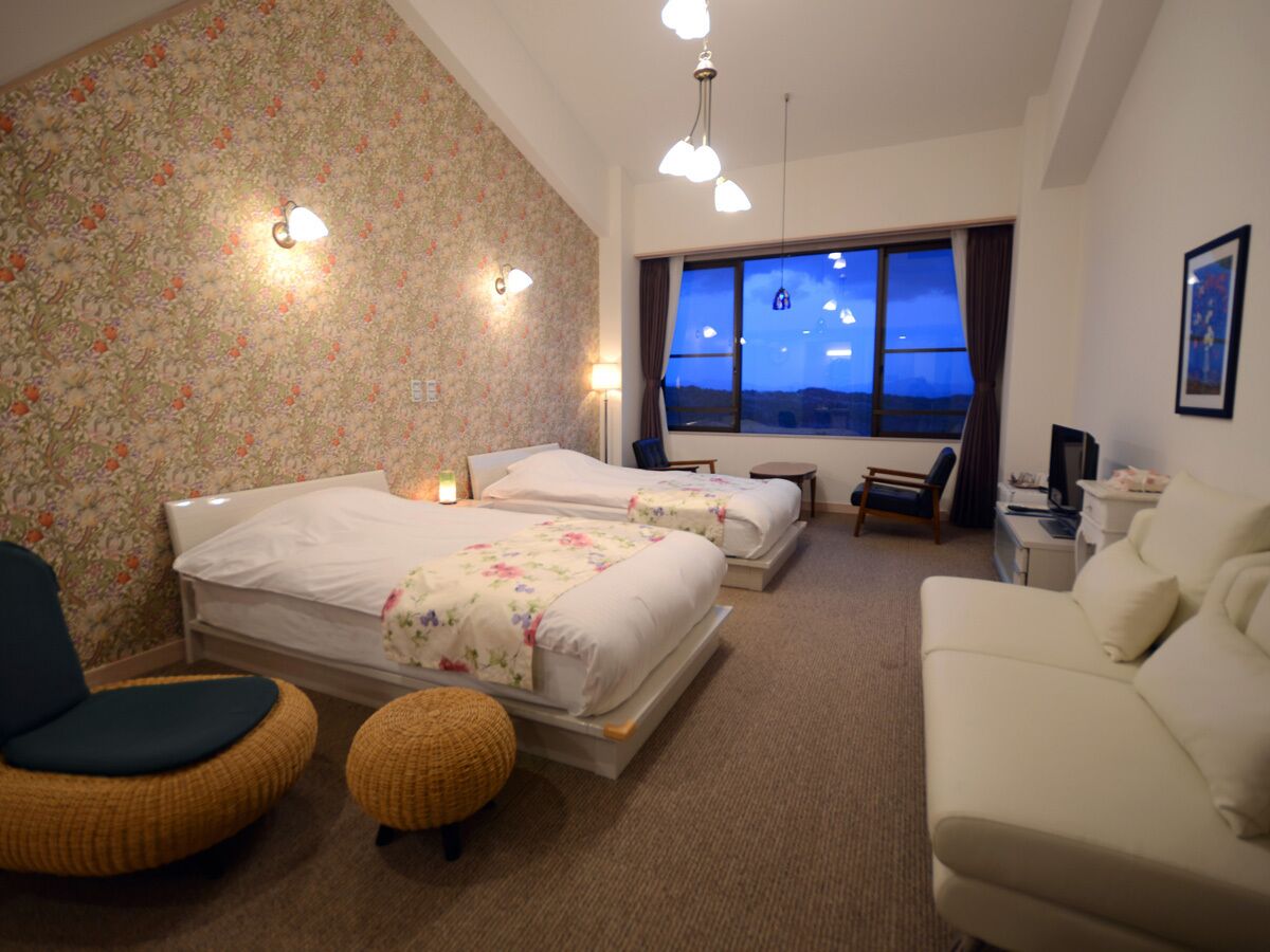 A hotel room with two beds, a sofa, a chair, a small table, and a TV.