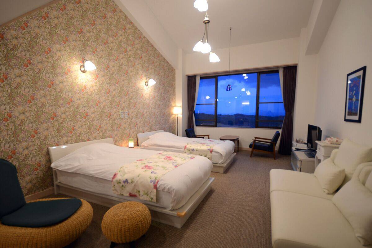 A hotel room with two beds, a sofa, a chair, a small table, and a TV.