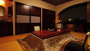 Ein traditioneller japanischer Raum mit Tatami-Böden, einem niedrigen Tisch mit Teeservice, Schiebetüren und einem Fernseher.