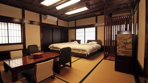 Ein traditioneller japanischer Raum mit Tatami-Boden, einem Holztisch, einem Bett mit weißer Bettwäsche und einer Schiebetür.