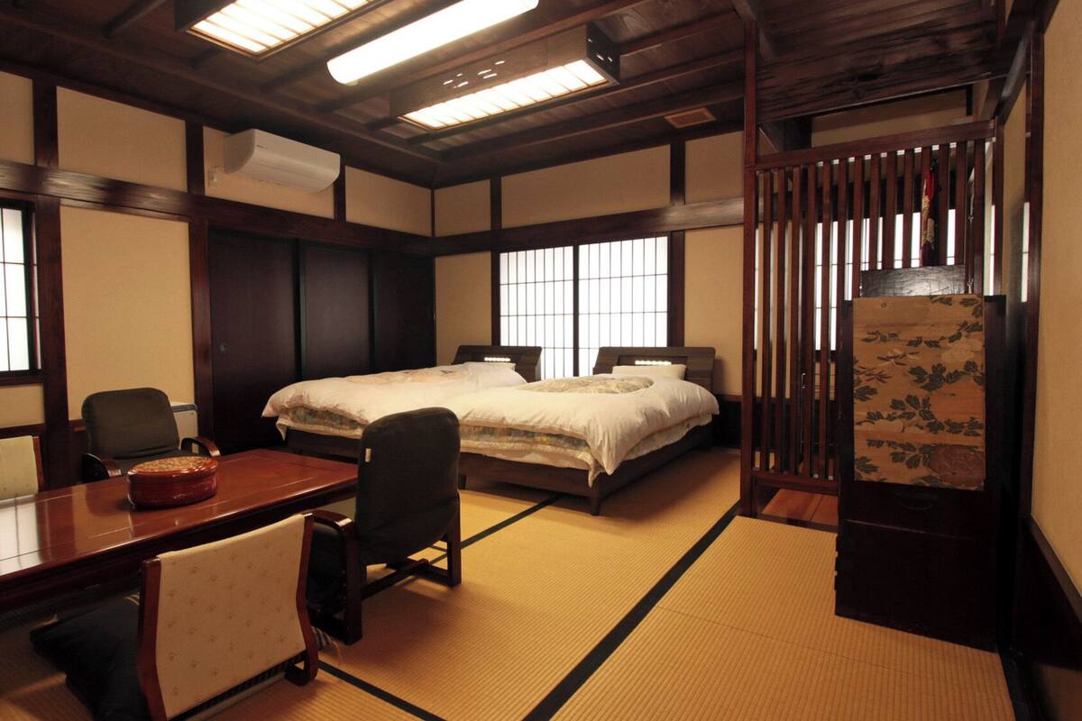 Une pièce de style japonais traditionnel, avec un sol recouvert de tatamis, un bureau en bois, un lit avec une literie blanche et des portes coulissantes.