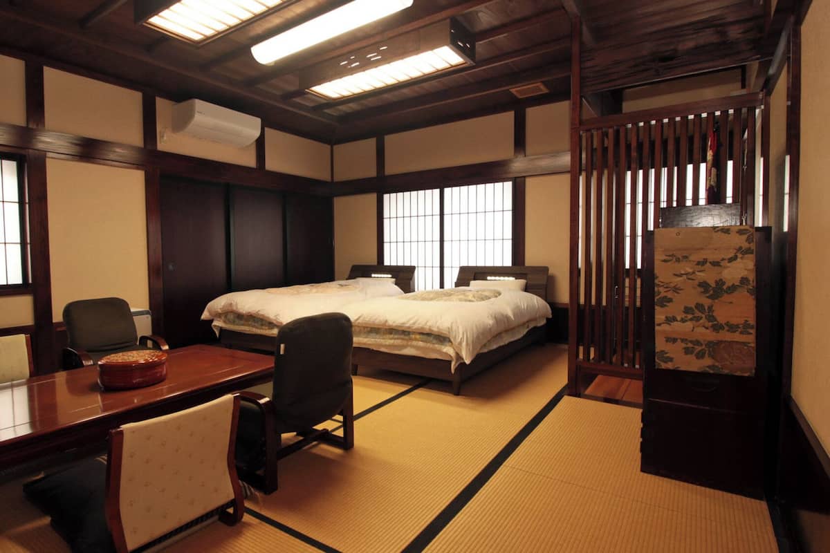 Perinteinen japanilaistyylinen huone, jossa on tatamimatto, puinen työpöytä, valkoisilla tekstiileillä varustettu sänky ja liukuvat ovet.