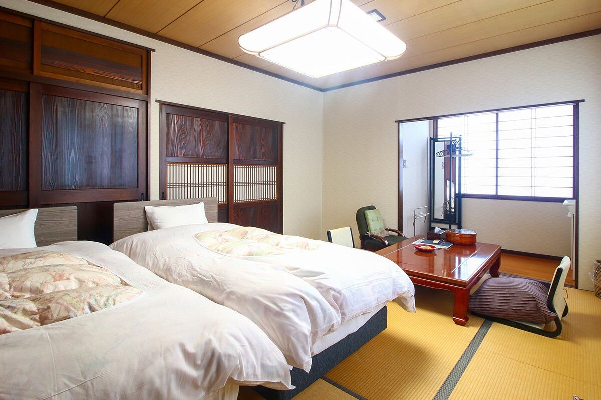 Een hotelkamer met twee bedden, een bureau, een stoel, een spiegel en een raam.
