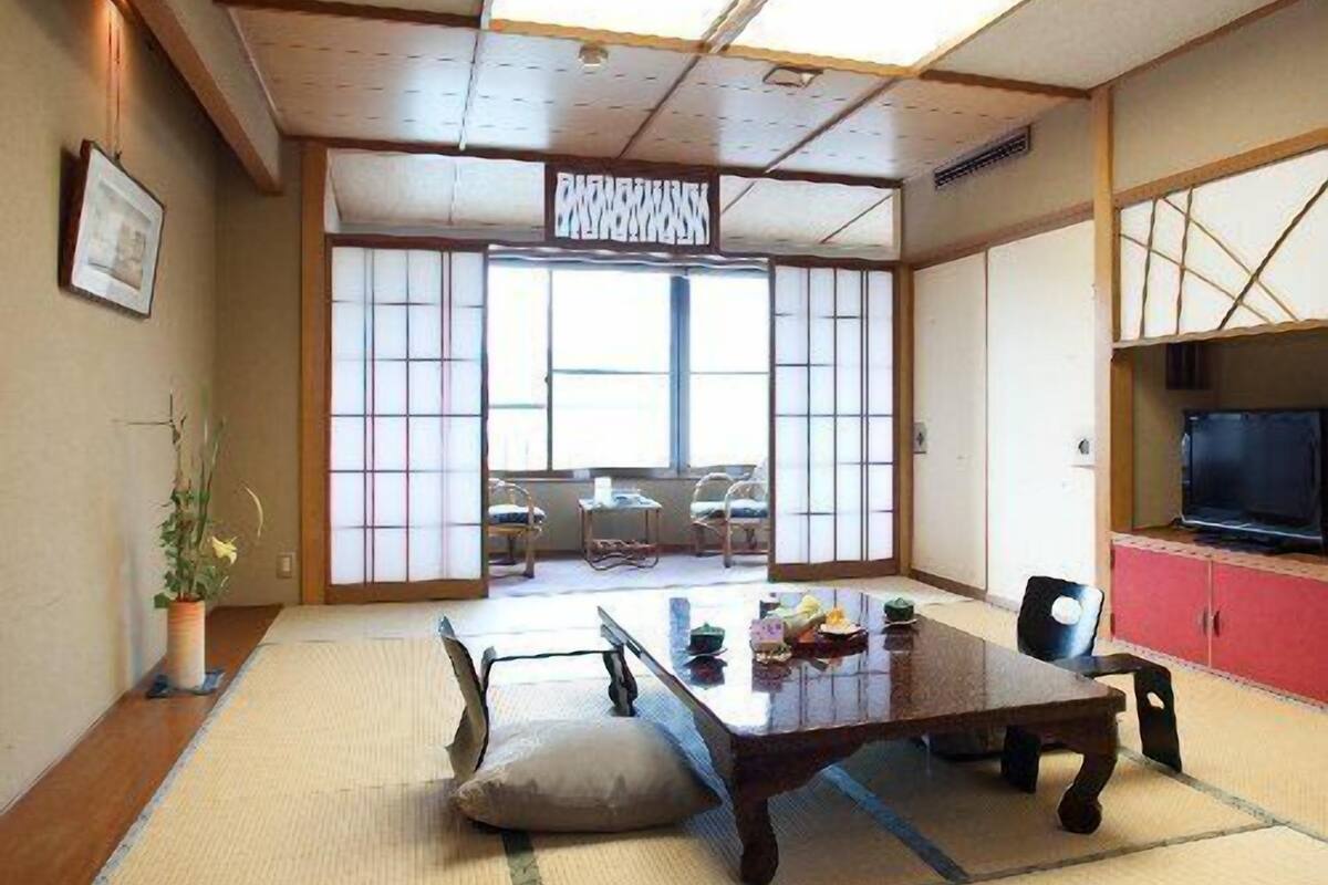 A traditional Japanese room with tatami flooring, a low table, chairs, a television, and sliding doors.