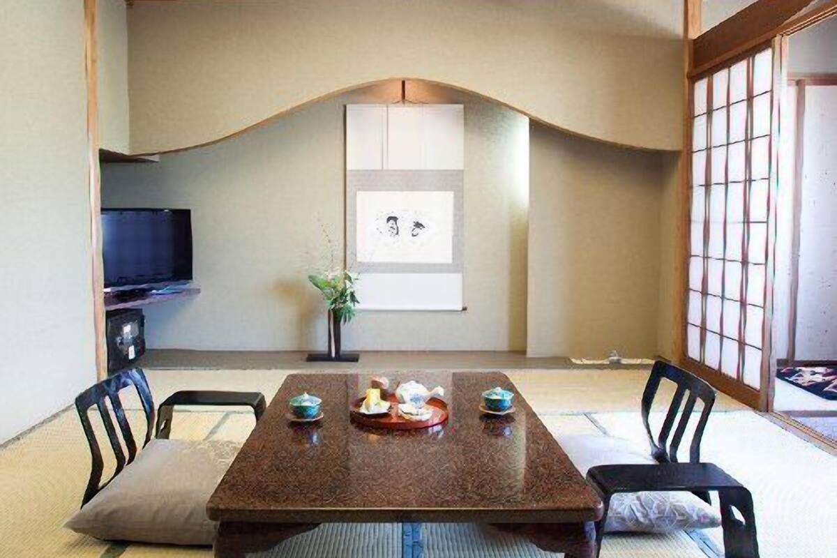 A traditional Japanese-style room with tatami flooring, a low table with a tray of items, and a television on the left.