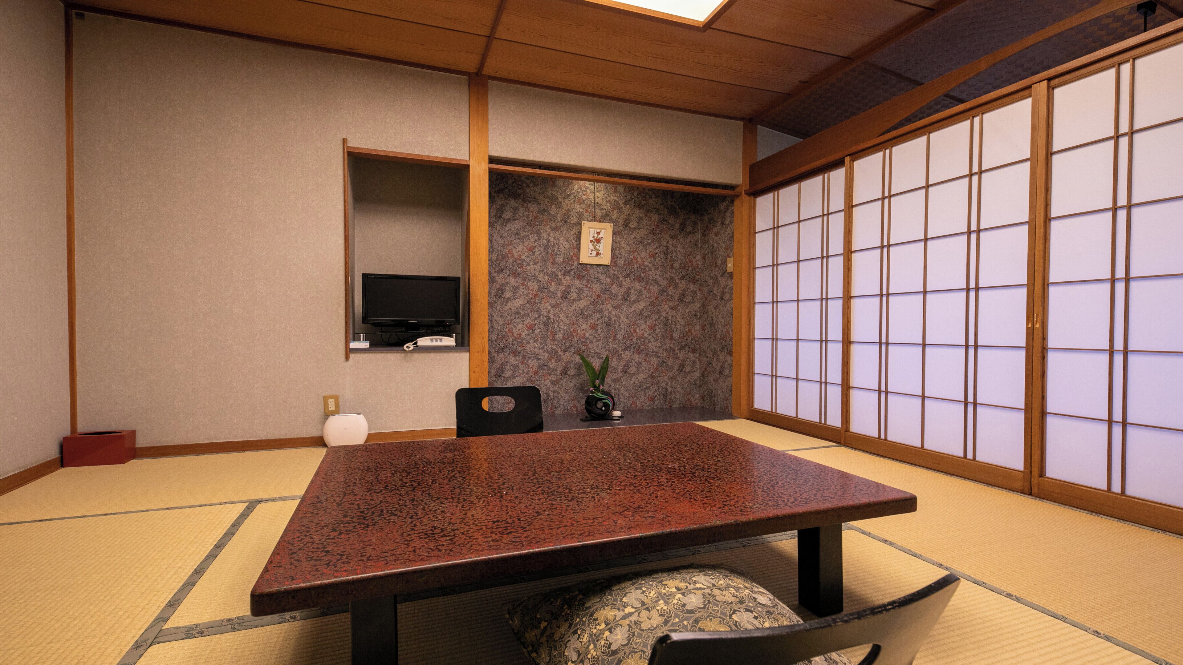 A traditional Japanese room with tatami flooring, a low table, a television, and a shoji screen.