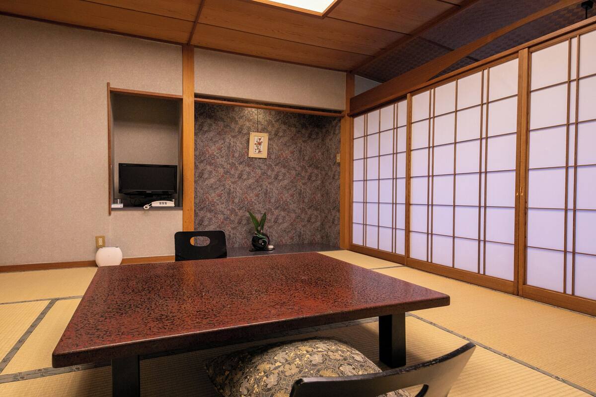 A traditional Japanese room with tatami flooring, a low table, a television, and a shoji screen.