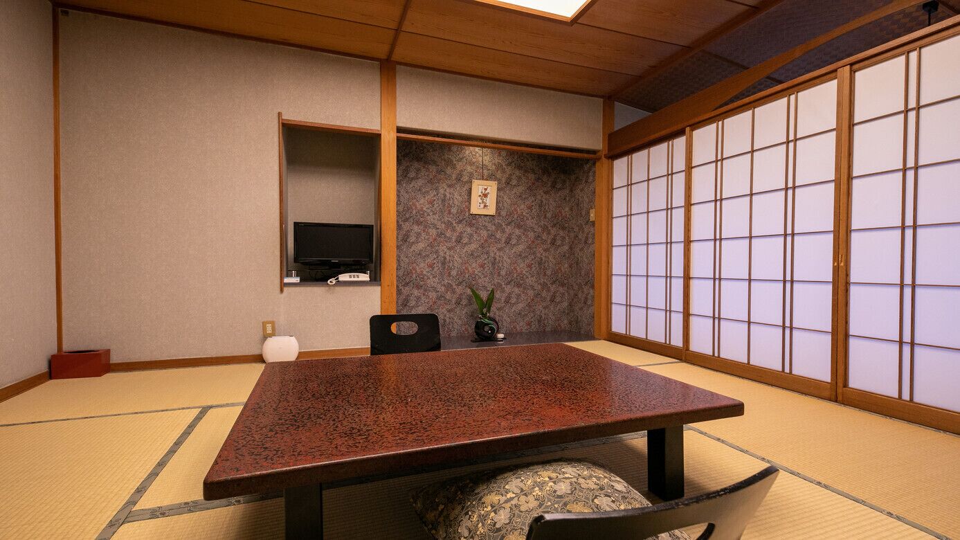 Ein traditioneller japanischer Raum mit Tatami-Böden, einem niedrigen Tisch, einem Fernseher und Shoji-Bildschirmen.