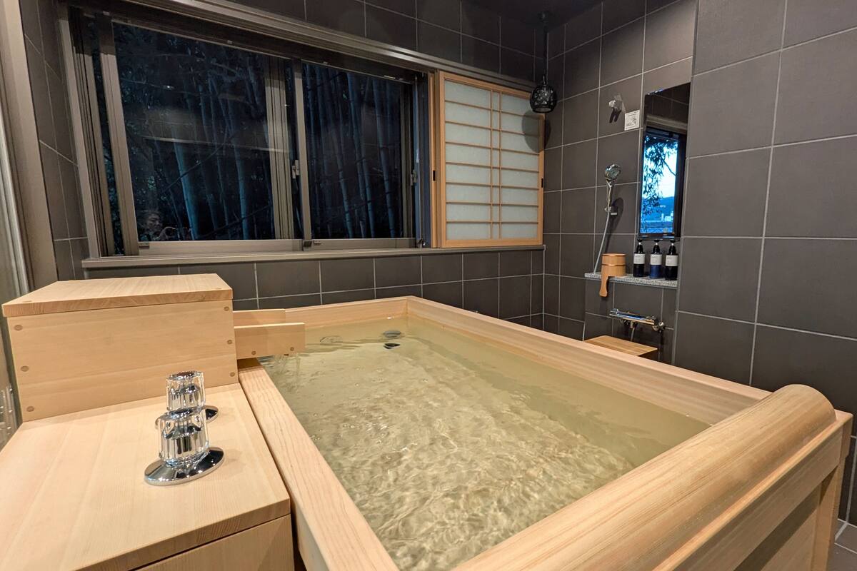 A modern bathroom with a wooden bathtub, a glass shower enclosure, and a window with a view.