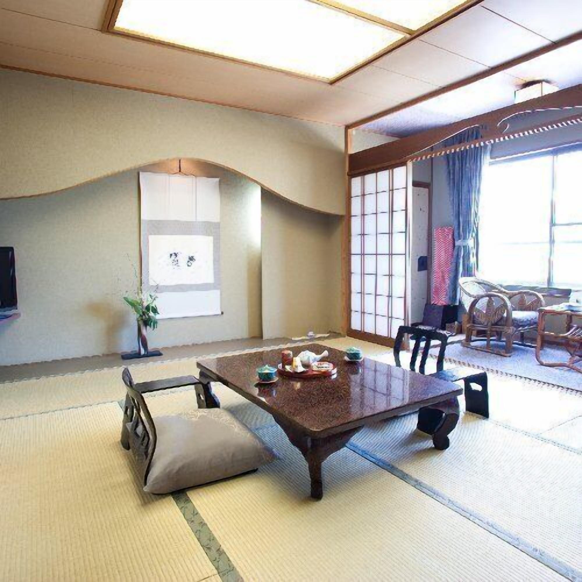A traditional Japanese room with tatami flooring, a low table with cushions, a TV, and a sliding door leading to a balcony with wicker furniture.