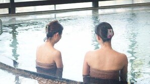 Two individuals in a pool with a view of a building and greenery outside. - Izunagaoka Onsen Ebisuya (Izunokuni)