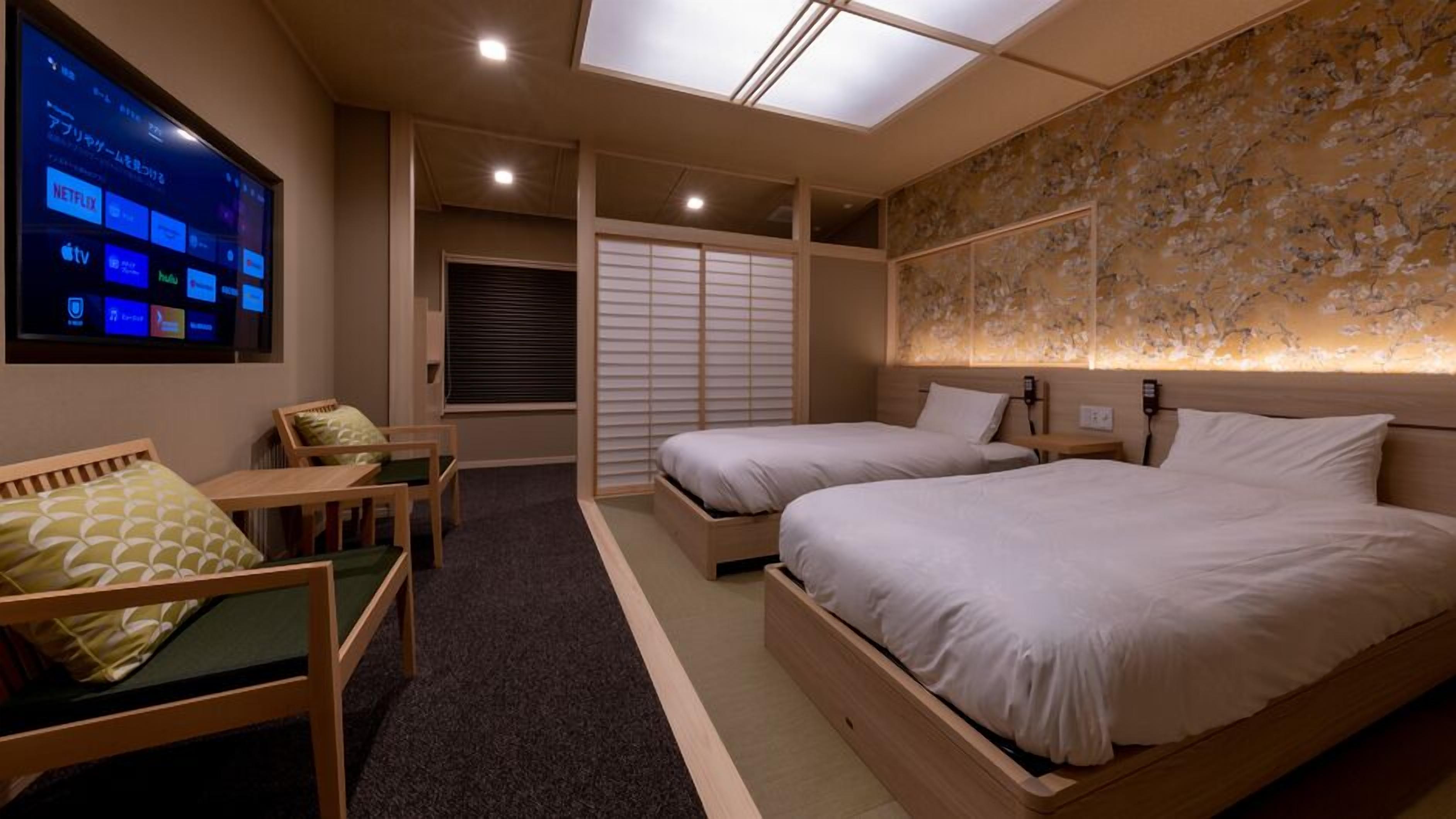Ein Hotelzimmer mit zwei Betten, einem Schreibtisch, einem Stuhl, einem Fernseher, der Streamingdienste anzeigt, und einem Dachfenster.