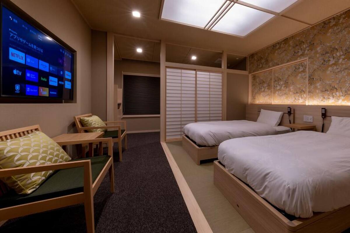 A hotel room with two beds, a desk, a chair, a TV displaying streaming services, and a skylight.