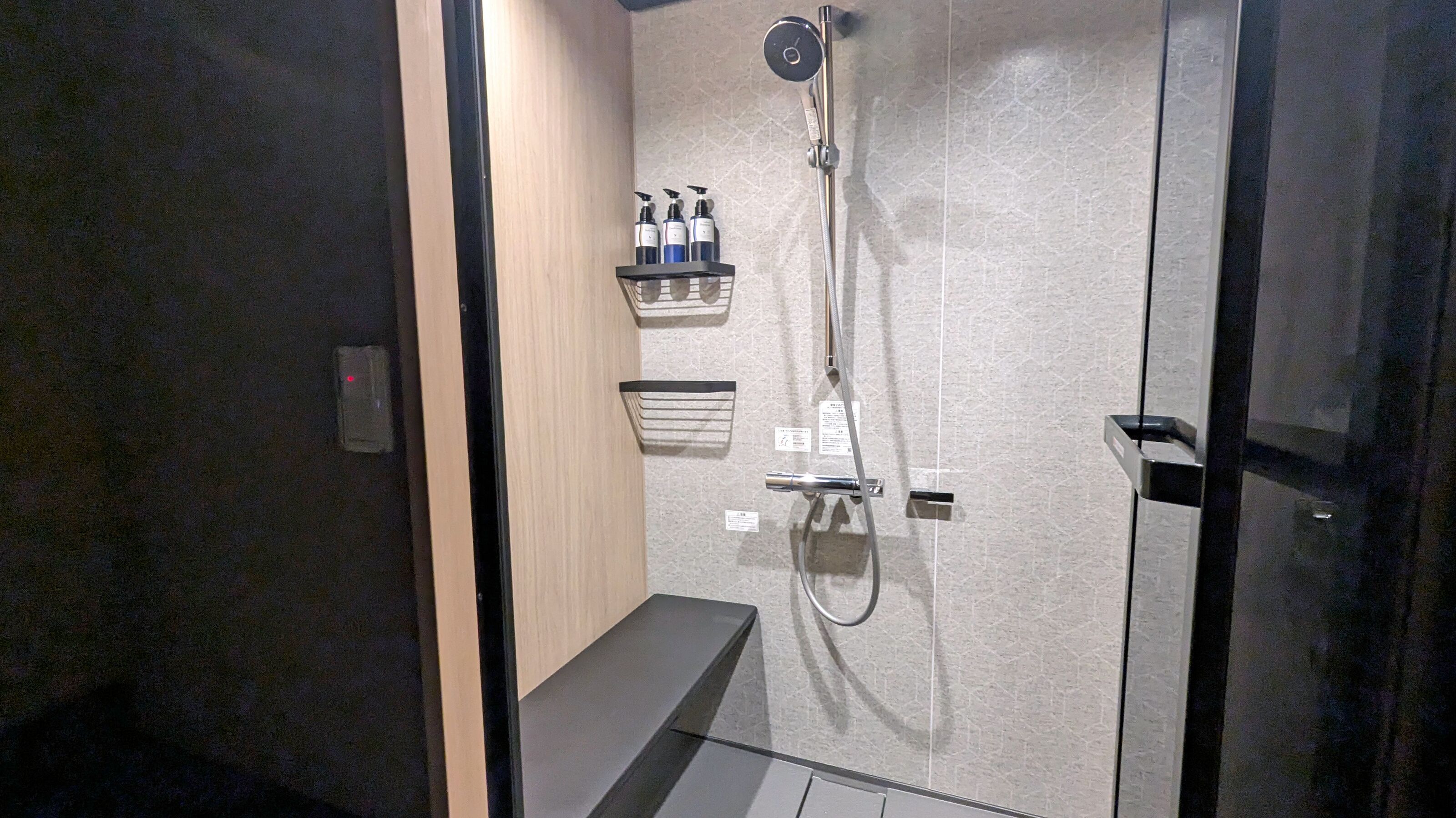 A modern shower with a handheld showerhead, a wall-mounted control panel, and a shelf with toiletries.