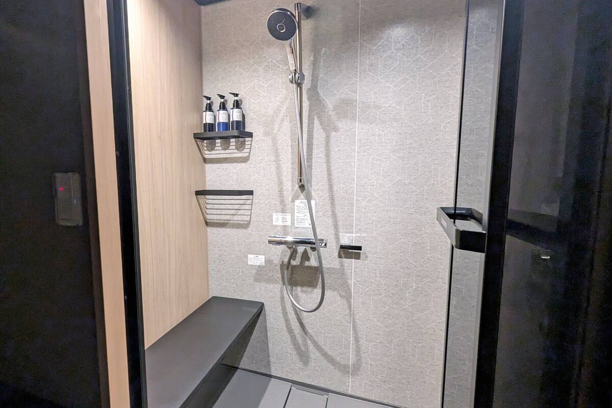 A modern shower with a handheld showerhead, a wall-mounted control panel, and a shelf with toiletries.