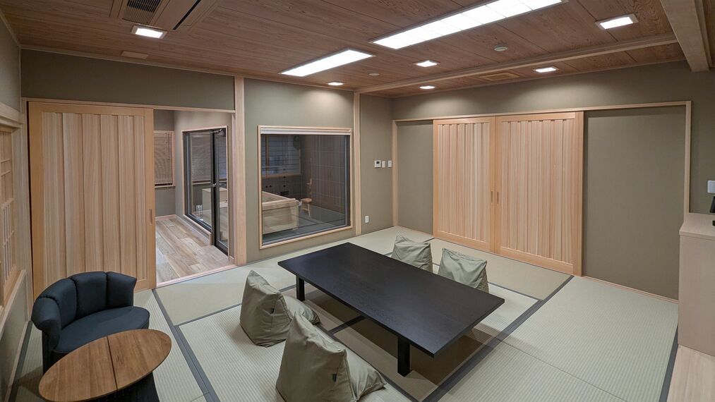 Ein Zimmer mit Tatami-Böden, einem niedrigen Tisch, einer Couch und Schiebetüren.