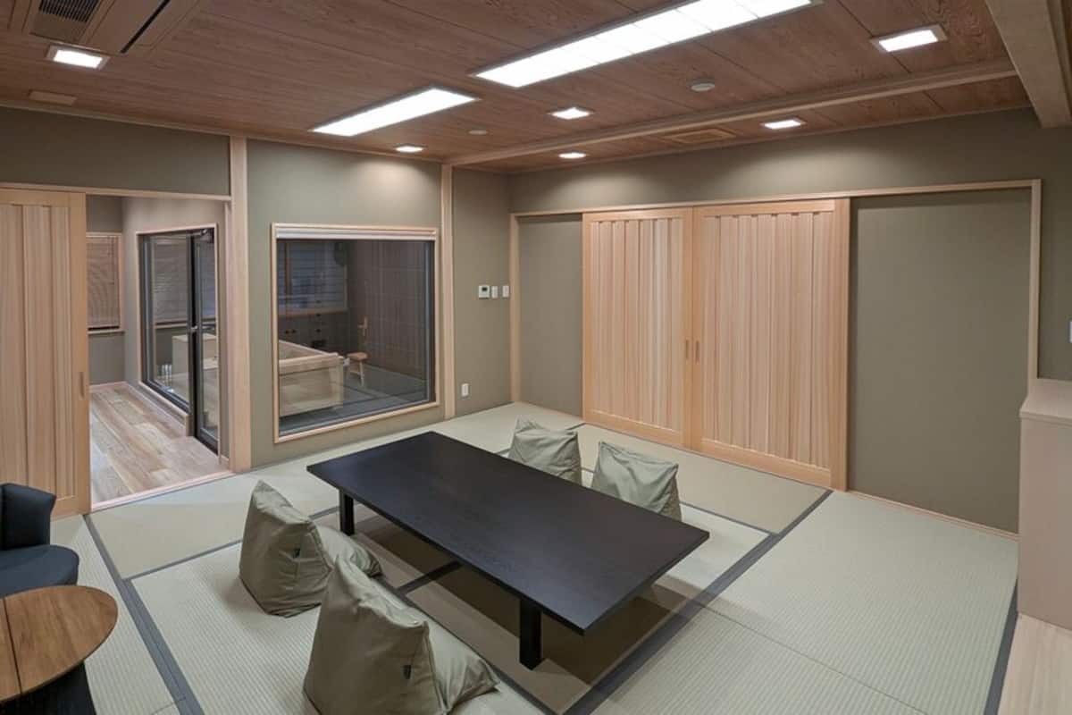 Ein Zimmer mit Tatami-Böden, einem niedrigen Tisch, einer Couch und Schiebetüren.