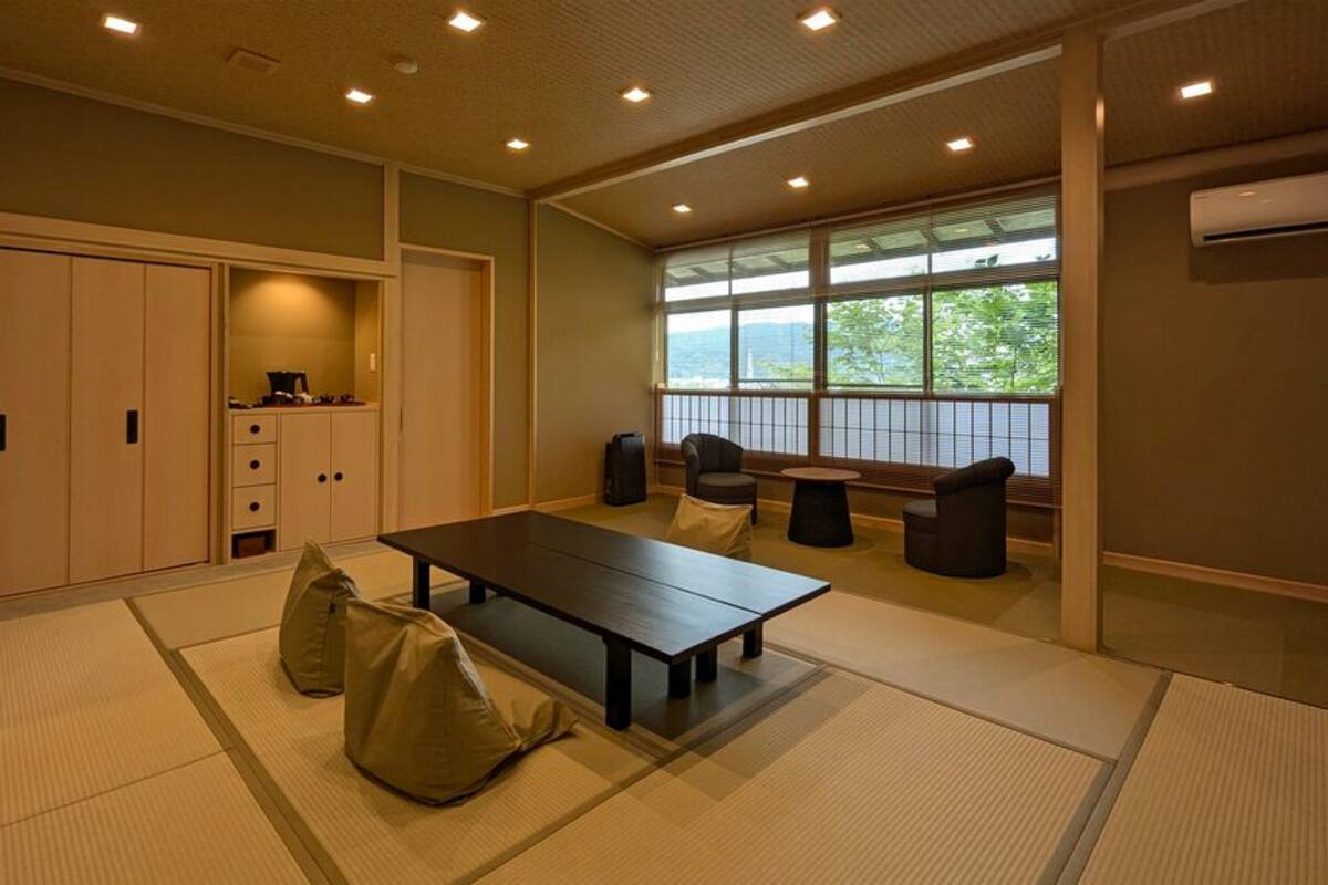 A room with tatami mats, a low table, chairs, a wardrobe, and a window with a view.