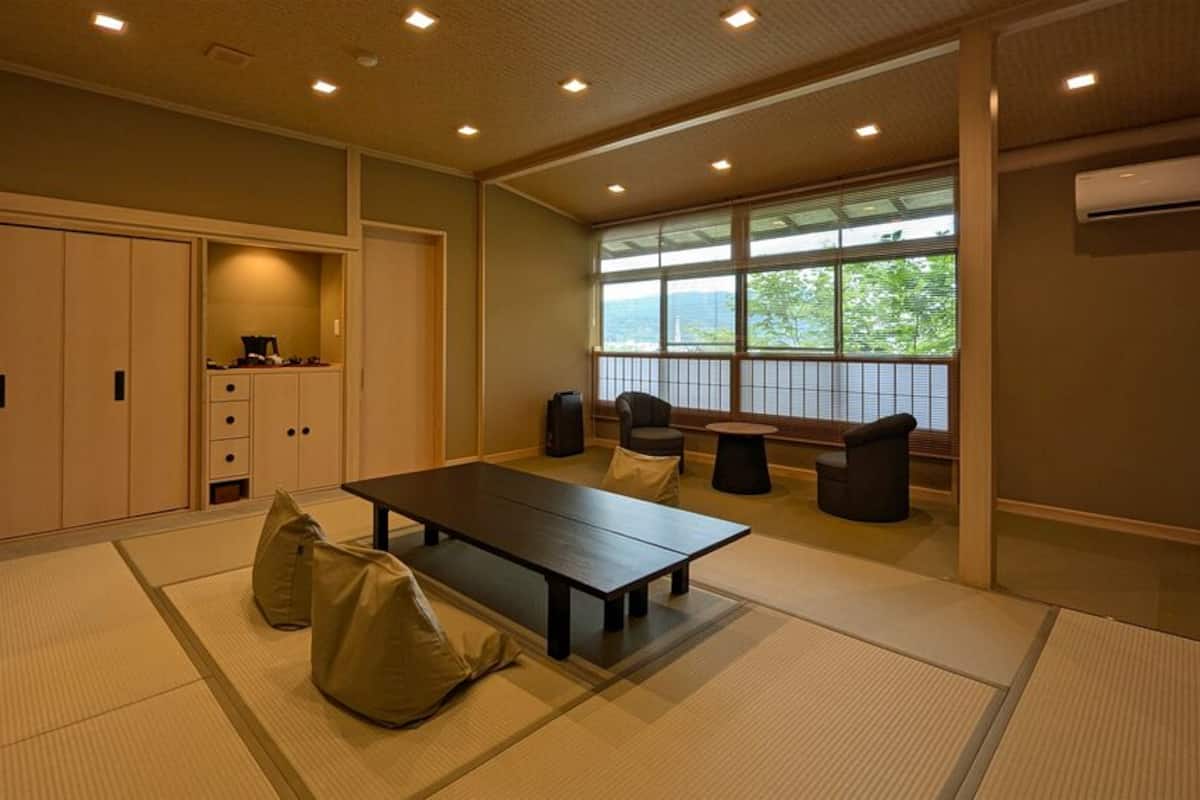Une pièce avec des tatamis, une table basse, des chaises, une armoire et une fenêtre donnant sur un paysage agréable.