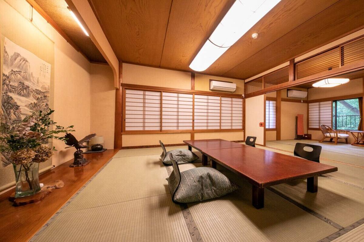 A traditional Japanese room with tatami flooring, a wooden table, tatami mats, a shoji screen, and a view of the outdoors.