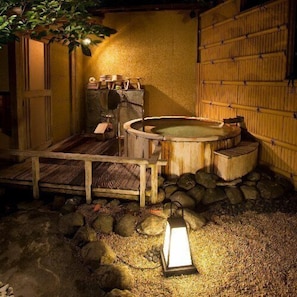 A traditional Japanese onsen with a wooden bath, stone steps, and a lantern.