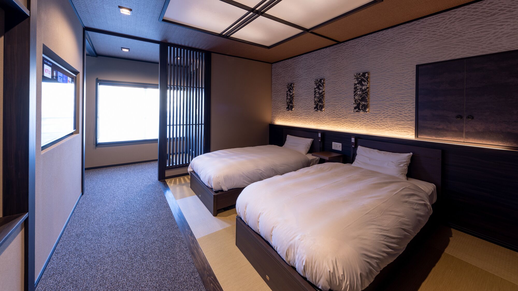 A modern hotel room with two beds, a large window, and a unique textured wall design.