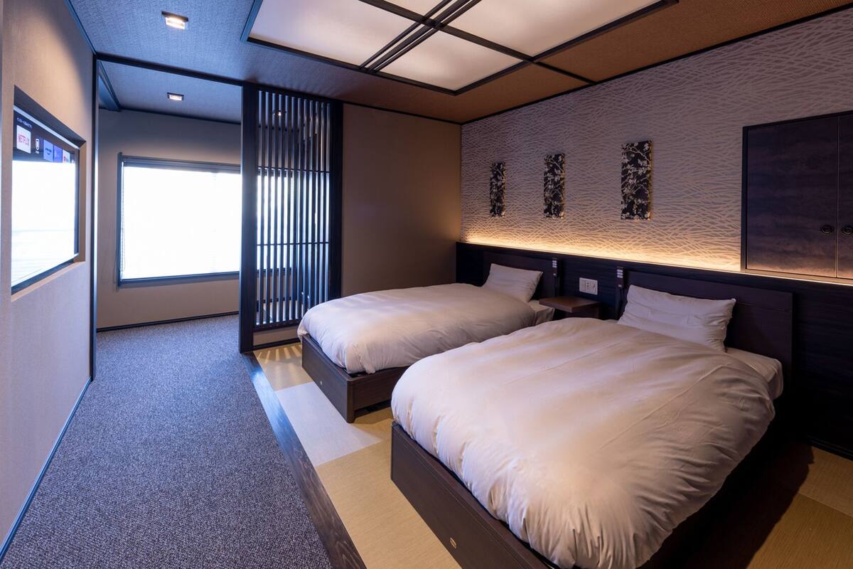 A modern hotel room with two beds, a large window, and a unique textured wall design.