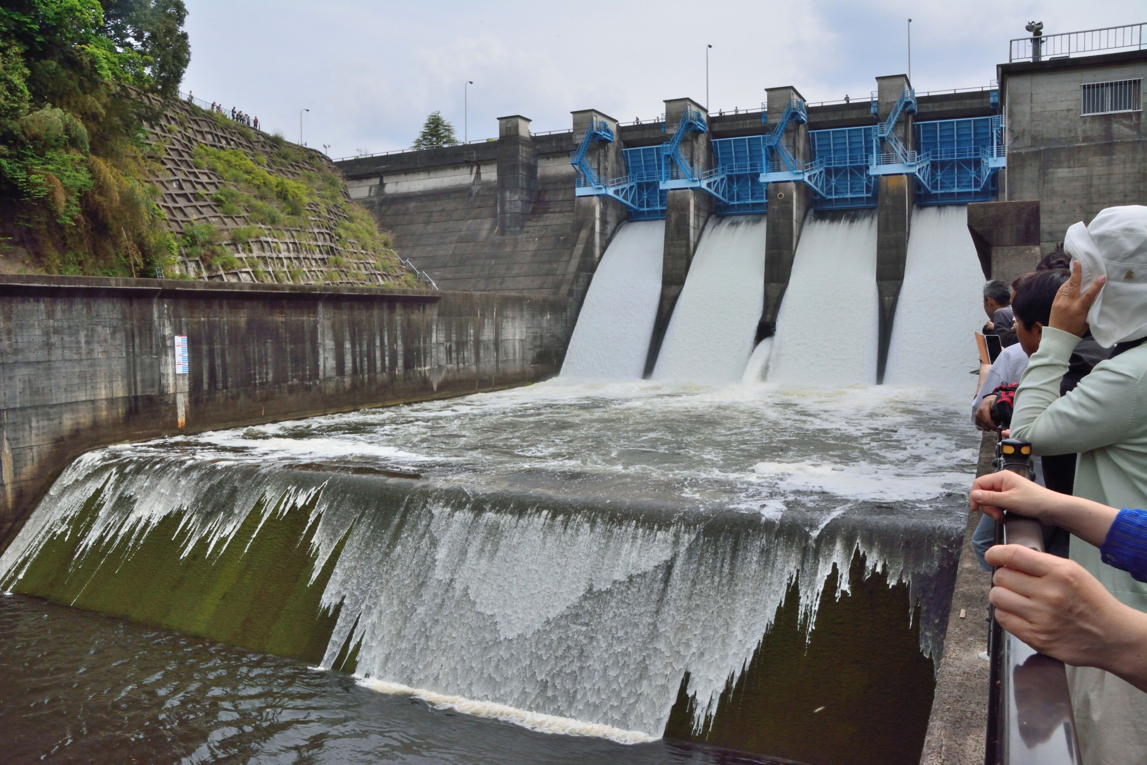 A dam with water flowing over it, a staircase, and people observing.