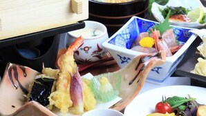 A variety of Japanese dishes including sushi, tempura, and a salad, served on traditional wooden and ceramic dishes.