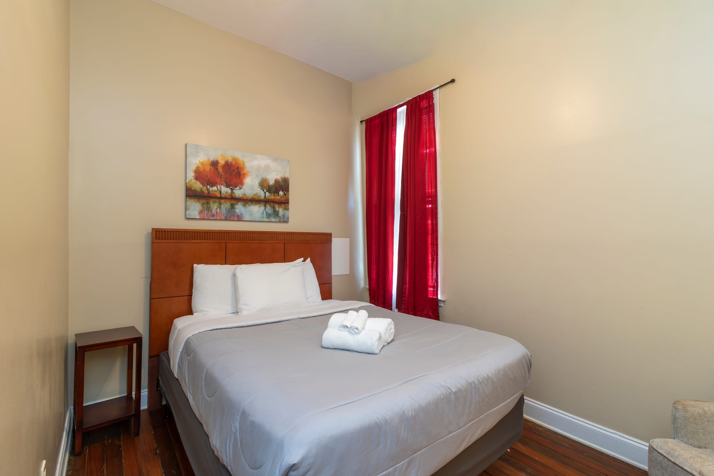 Une chambre d’hôtel avec un grand lit, une table de chevet, un tableau au mur et des rideaux rouges.