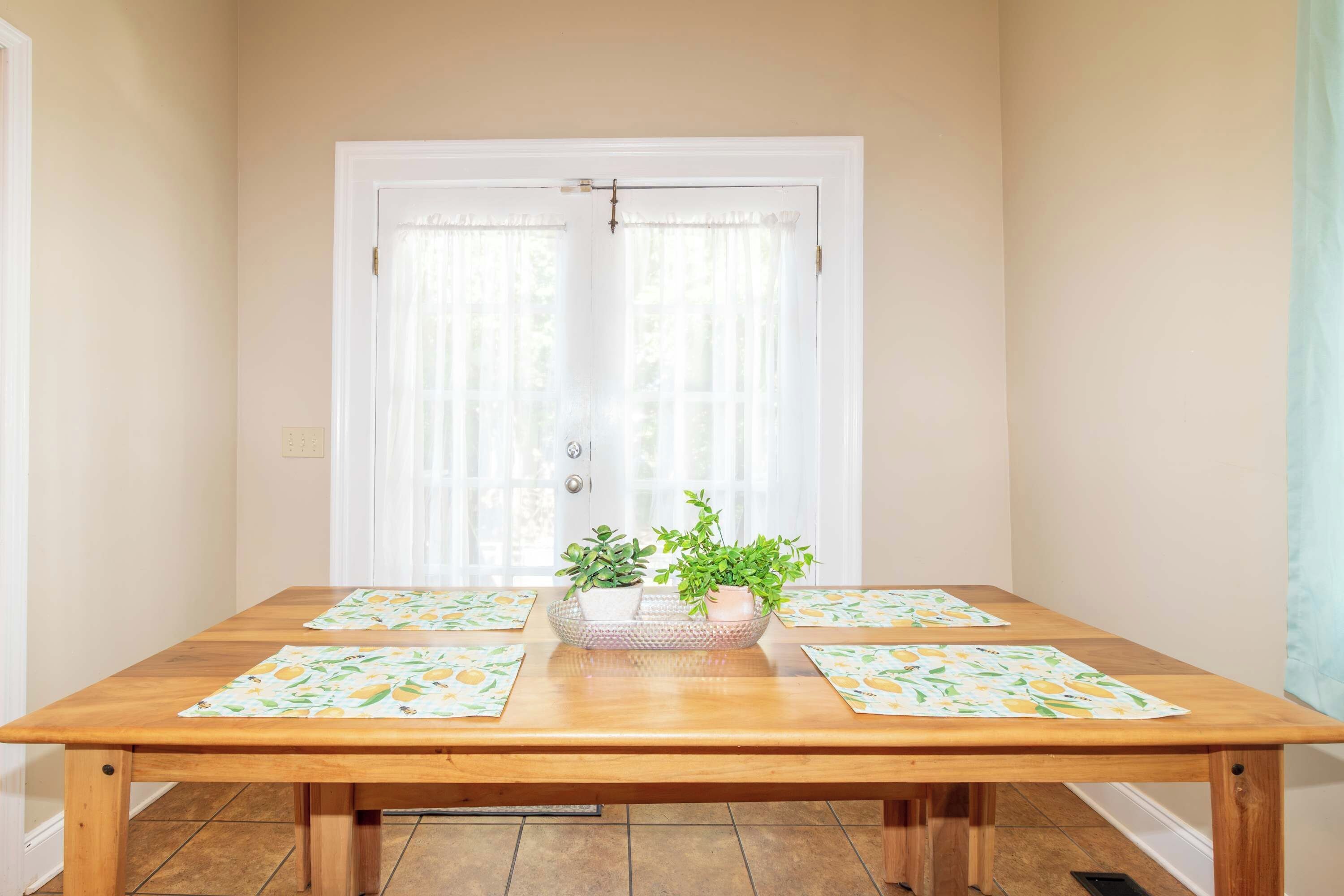 Mesa de jantar com duas plantas em vasos e jogos americanos combinando.