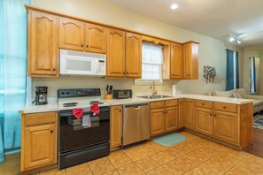 A kitchen with wooden cabinets, a microwave, a stove, a dishwasher, and a sink. - Closest Historic BnB to Ft Moore-Americana Cottage (Columbus)