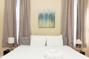 A hotel room with a bed, two nightstands, a lamp on each, and a painting on the wall. - Closest Historic BnB to Ft Moore-Americana Cottage (Columbus)