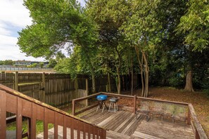 Una terraza de madera con una parrilla y zona de estar, rodeada de árboles.